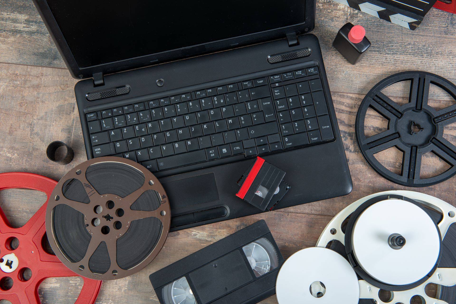 Laptop umgeben von alten Filmrollen, VHS-Kassetten und digitalen Speichermedien, bereit zur Digitalisierung und Konvertierung von VHS-Aufnahmen in digitale Formate.