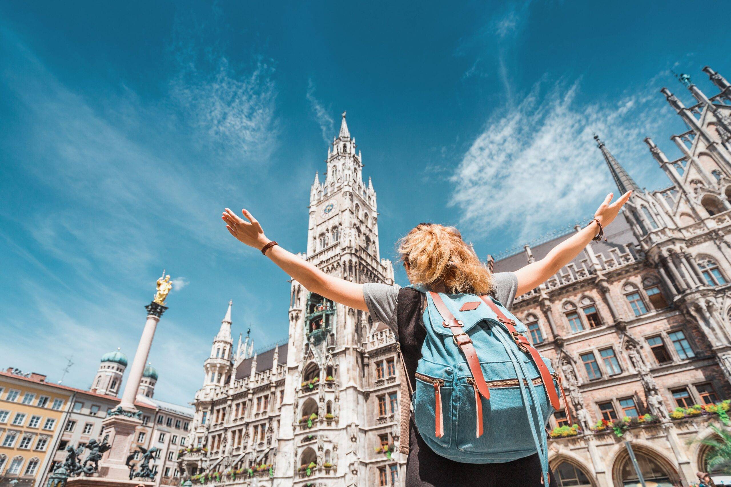 Junge Person mit Rucksack vor dem Neuen Rathaus in München mit offenen Armen bei sonnigem Wetter