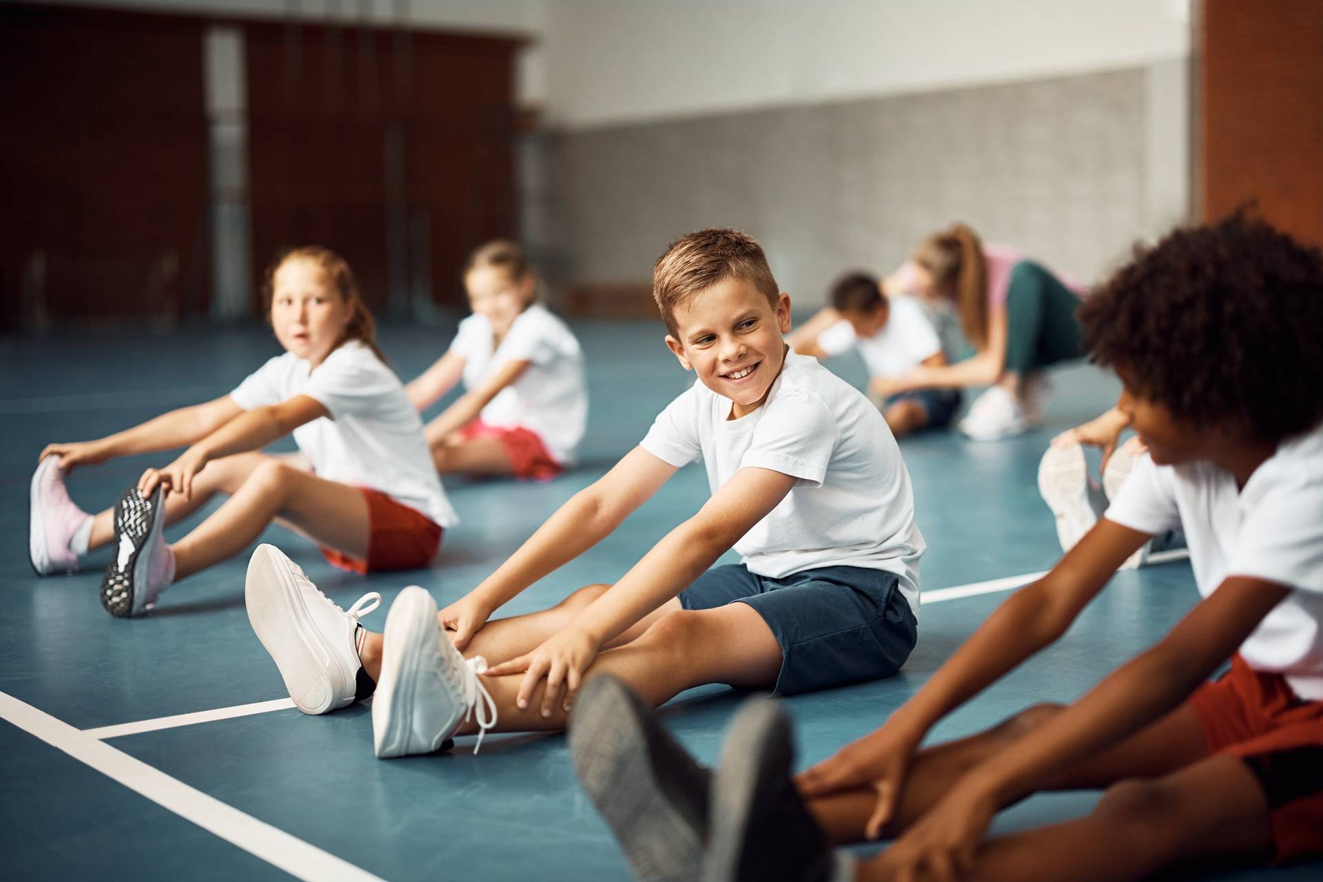 Kinder dehnen sich im Sportunterricht in der Halle | Kinderkarate München